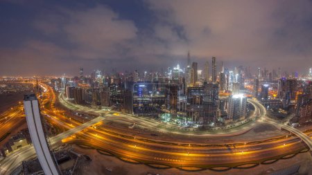 Foto de Skyline panorámico de Dubai con bahía de negocios y distrito céntrico noche a día timelapse transición. Vista aérea de gran angular de muchos rascacielos modernos durante el amanecer con reflejos de vidrio. Emiratos Árabes Unidos. - Imagen libre de derechos