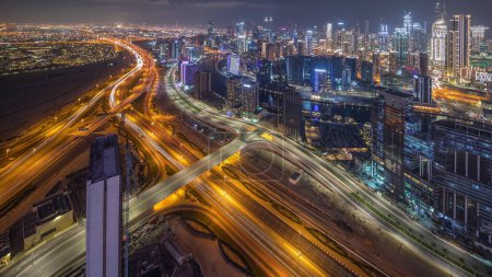 Foto de Panorama que muestra el horizonte de Dubái con la bahía de negocios y el timelapse de la noche del distrito centro. Vista aérea de muchos rascacielos modernos y tráfico ocupado en la carretera al khail. Emiratos Árabes Unidos. - Imagen libre de derechos