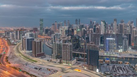 Foto de Skyline con la arquitectura moderna de Dubai business bay iluminado torres noche a día timelapse transición. Vista panorámica aérea con canal y sitio de construcción antes del amanecer - Imagen libre de derechos