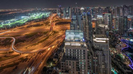 Foto de Panorama que muestra el puerto deportivo de Dubái y los rascacielos iluminados JLT a lo largo de Sheikh Zayed Road con un enorme cruce y un timelapse nocturno aéreo del distrito de los medios de comunicación. Edificios residenciales y de oficinas desde arriba. - Imagen libre de derechos