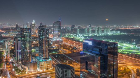 Foto de Luna subiendo sobre los medios de comunicación de la ciudad y al barsha alturas zona de distrito noche timelapse aéreo desde Dubai marina. Torres y rascacielos con tráfico en una carretera desde arriba - Imagen libre de derechos