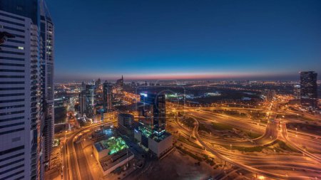 Foto de Vista panorámica aérea de la ciudad de los medios de comunicación y el distrito de alturas al barsha con campo de golf noche a día timelapse transición desde el puerto deportivo de Dubai. Torres y rascacielos con tráfico en una intersección de carreteras desde arriba - Imagen libre de derechos