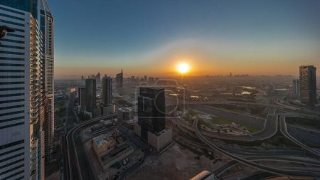 Foto de Salida del sol sobre la ciudad de los medios de comunicación y al barsha alturas distrito aéreo timelapse panorámica desde Dubai marina. Torres y rascacielos con campo de golf y tráfico en una intersección de carreteras desde arriba - Imagen libre de derechos