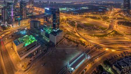 Téléchargez les photos : Vue panoramique aérienne de la ville des médias et du quartier d'al barsha Heights avec parcours de golf de nuit au jour passage timelapse de la marina de Dubaï pendant le lever du soleil. Tours et gratte-ciel avec circulation sur un carrefour routier par le haut - en image libre de droit