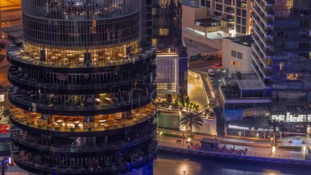 Téléchargez les photos : Dubaï port de plaisance front de mer et bâtiment avec différents restaurants à chaque étage aérien nuit au jour passage timelapse. Creek, yachts avec jetée et gratte-ciel autour avant le lever du soleil - en image libre de droit