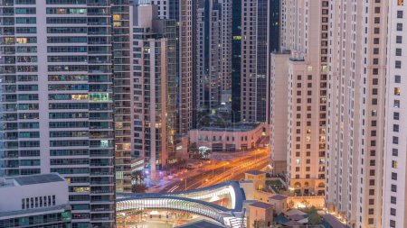 Photo for Overview to JBR and Dubai Marina skyline with modern high rise skyscrapers waterfront living apartments aerial night to day transition timelapse. Traffic on road intersection and footbridge - Royalty Free Image