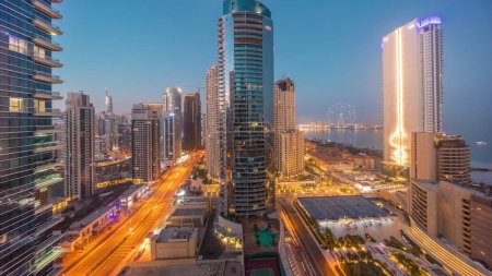 Foto de Vista panorámica de la Marina de Dubái y la zona de JBR y la famosa rueda de la fortuna noche aérea al día timelapse transición y rascacielos iluminados antes del amanecer - Imagen libre de derechos