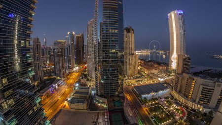 Foto de Panorama de la zona de Dubai Marina y JBR y la famosa rueda de la fortuna noche aérea al día timelapse transición. Rascacielos iluminados durante el amanecer con largas sombras - Imagen libre de derechos