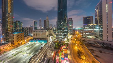Photo for Dubai International Financial district night to day transition timelapse. Panoramic aerial view of business office towers before sunrise. Illuminated skyscrapers with hotels and parking lot - Royalty Free Image
