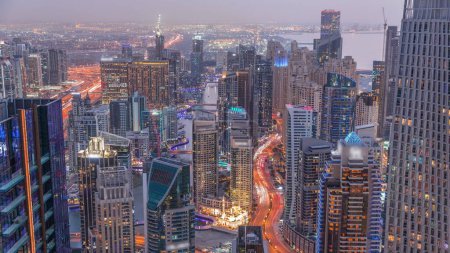 Foto de Vista panorámica del horizonte de Dubai Marina y JBR que muestra el canal rodeado de rascacielos iluminados a lo largo de la línea aérea de la costa día a noche timelapse transición. Tráfico en carretera curva después del atardecer. DUBAI, Emiratos Árabes Unidos - Imagen libre de derechos