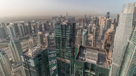 Foto de Panorama mostrando Dubai Marina y JLT con el distrito JBR por la mañana. Tráfico en carretera entre rascacielos timelapse aéreo. Modernas torres y obras de construcción. Yates flotando en el puerto - Imagen libre de derechos