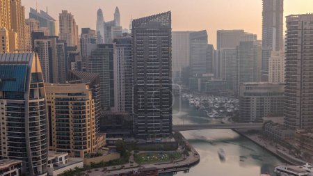 Photo for Dubai Marina with boats and yachts parked in harbor and skyscrapers around canal aerial morning timelapse during sunrise. Towers along waterfront with warm light - Royalty Free Image