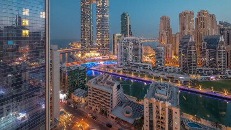 Foto de Dubai Marina rascacielos y el distrito JBR antes del amanecer con edificios de lujo iluminados y resorts noche aérea al día timelapse transición. Frente al mar con palmeras y barcos flotando en el canal - Imagen libre de derechos