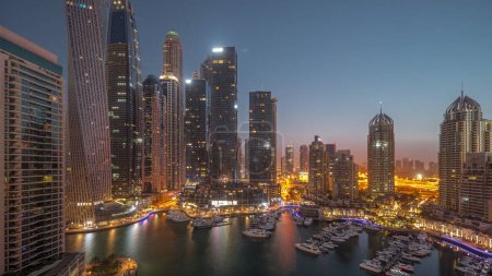 Photo for Dubai marina tallest skyscrapers and yachts in harbor aerial night to day transition timelapse during sunrise. View at apartment buildings, hotels and office blocks, modern residential development of UAE - Royalty Free Image