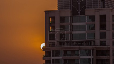 Foto de Salida del sol sobre el distrito turístico de lujo de Dubai Marina con salida del sol detrás del timelapse aéreo del rascacielos. Edificios incidenciales y cielo naranja - Imagen libre de derechos