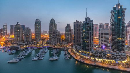 Téléchargez les photos : Baie de yacht de luxe dans la ville aérienne nuit au jour passage timelapse dans la marina de Dubaï avant le lever du soleil. Des gratte-ciel modernes le long de la promenade riveraine et des bateaux flottant dans le port - en image libre de droit