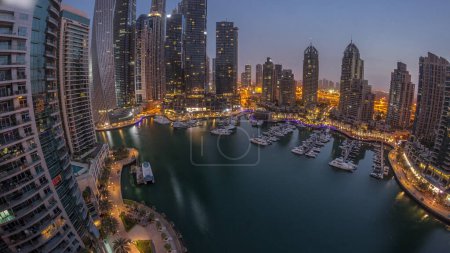 Dubai marina tallest skyscrapers and yachts in harbor aerial night to day transition panoramic timelapse before sunrise. View at apartment buildings, hotels and office blocks, modern residential development of UAE