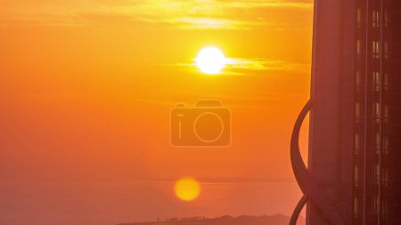 Téléchargez les photos : Coucher de soleil sur la mer près du canal d'eau de Dubaï avec ciel orange timelapse aérienne. Vue de dessus derrière le gratte-ciel - en image libre de droit