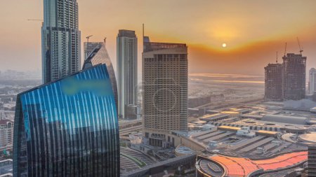 Foto de Aerial sunrise panorama del centro de Dubai con centro comercial y el tráfico en una calle mañana timelapse desde arriba, Emiratos Árabes Unidos. Rascacielos y hoteles modernos. Cielo naranja - Imagen libre de derechos