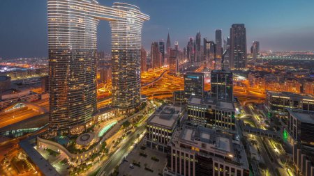 Foto de Futuristic Dubai Downtown and finansial district skyline aerial night to day transition timelapse. Muchas torres y rascacielos con tráfico en las calles durante la salida del sol con reflejos solares - Imagen libre de derechos