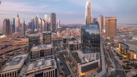 Téléchargez les photos : Futuriste Dubai Downtown and finansial district skyline panorama aérien du jour à la nuit transition timelapse. Nombreuses tours éclairées et gratte-ciel avec circulation dans les rues - en image libre de droit