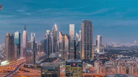 Téléchargez les photos : Panorama du quartier du centre financier de Dubaï avec de grands gratte-ciel avec éclairage jour à nuit transition timelapse. Vue aérienne vers les tours le long de l'autoroute animée après le coucher du soleil - en image libre de droit