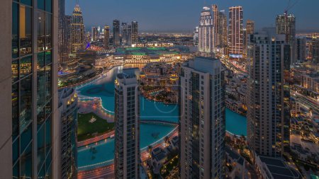 Foto de Vista aérea de una gran ciudad futurista con lago y fuentes día a noche timelapse transición. Bahía de negocios y distrito centro con muchos rascacielos y casas tradicionales, Dubai, Emiratos Árabes Unidos skyline. - Imagen libre de derechos