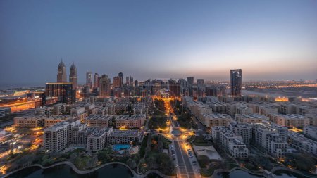 Téléchargez les photos : Panorama des gratte-ciel dans le quartier de Barsha Heights et des immeubles de faible hauteur dans le quartier des Verts timelapse de transition aérienne de nuit au jour. Skyline de Dubaï avec circulation dans les rues éclairées - en image libre de droit