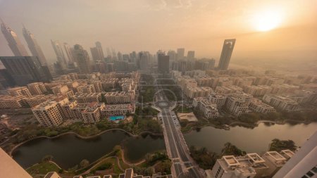 Foto de El amanecer sobre los rascacielos en el distrito de Barsha Heights y los edificios de poca altura en el timelapse aéreo del distrito de Greens miran hacia abajo durante todo el día. Dubai skyline con el tiempo brumoso y las sombras moviéndose rápido - Imagen libre de derechos