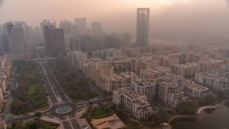 Téléchargez les photos : Des gratte-ciel dans le quartier de Barsha Heights et des immeubles de faible hauteur dans le quartier des Verts se succèdent au lever du soleil. Skyline de Dubaï avec ciel orange au matin brumeux - en image libre de droit