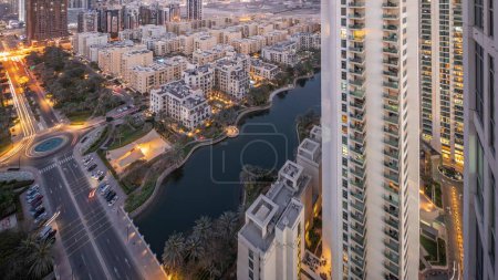 Téléchargez les photos : Bâtiments d'étang et de faible hauteur dans le quartier des Verts timelapse de transition aérienne de jour à nuit. Skyline de Dubaï avec des gratte-ciel dans le quartier de Barsha Heights sur un fond - en image libre de droit