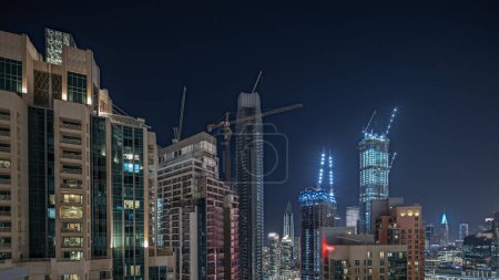 Foto de Panorama mostrando paisaje urbano aéreo nocturno timelapse con arquitectura iluminada del centro de Dubái. Muchos rascacielos altos y torres con ventanas brillantes. Nuevo sitio de construcción. - Imagen libre de derechos