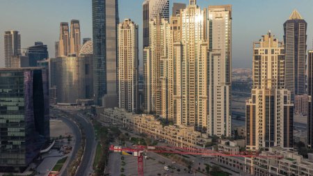 Foto de Bay Avenue durante el amanecer con torres modernas desarrollo residencial en Business Bay timelapse aéreo, Dubai, Emiratos Árabes Unidos. Rascacielos con reflejos solares de superficie de vidrio - Imagen libre de derechos