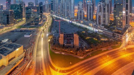 Téléchargez les photos : Bay Avenue avec des tours modernes développement résidentiel à Business Bay panoramique aérienne nuit à la transition quotidienne timelapse, Dubaï, EAU. gratte-ciel avec circulation sur une route près d'un grand parking - en image libre de droit