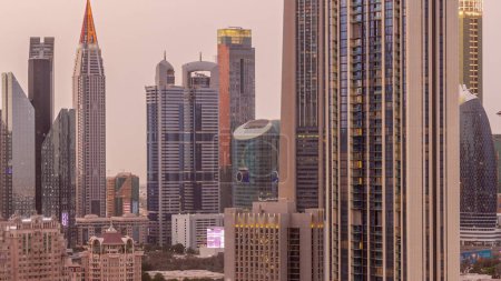 Téléchargez les photos : Rangée des grands bâtiments autour de Sheikh Zayed Road et DIFC district aérien jour à nuit timelapse transition à Dubaï, Émirats arabes unis. gratte-ciel International Financial Centre avec surface vitrée - en image libre de droit