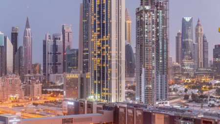 Foto de Panorama de edificios altos alrededor de Sheikh Zayed Road y DIFC distrito aéreo noche al día timelapse transición en Dubai, Emiratos Árabes Unidos. Rascacielos del Centro Financiero Internacional con superficie de vidrio antes del amanecer - Imagen libre de derechos