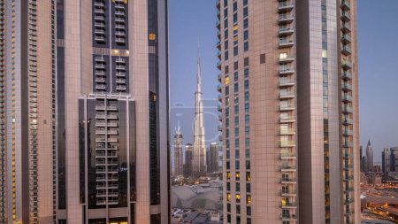 Téléchargez les photos : Les plus hauts gratte-ciel du centre-ville de Dubai situé sur la rue bouleward près du centre commercial aérien nuit à la transition de jour timelapse. Soleil réfléchi par la surface du verre au lever du soleil - en image libre de droit