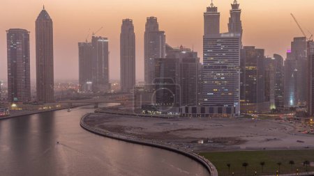 Téléchargez les photos : Paysage urbain de gratte-ciel à Dubai Business Bay avec canal d'eau aérien jour à nuit passage timelapse. Skyline moderne avec tours et front de mer après le coucher du soleil. Un centre d'affaires international - en image libre de droit