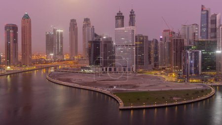 Téléchargez les photos : Paysage urbain de gratte-ciel dans la baie d'affaires de Dubaï avec péninsule sur canal d'eau passage aérien nuit à jour timelapse avec la lune couchant. Skyline moderne avec tours éclairées et front de mer avant le lever du soleil - en image libre de droit