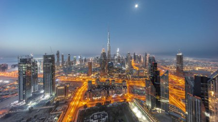 Foto de Vista aérea de las torres más altas de Dubái Centro skyline noche a día timelapse transición antes del amanecer. Distrito financiero y área de negocios en la ciudad urbana inteligente con Luna. Rascacielos y edificios de gran altura - Imagen libre de derechos