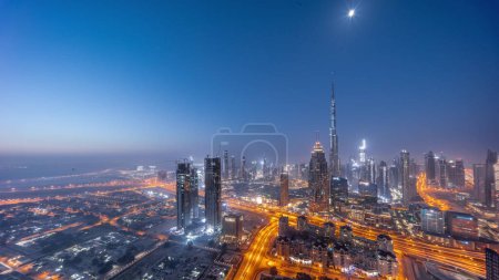 Aerial panoramic view of tallest towers in Dubai Downtown skyline night to day transition timelapse before sunrise. Financial district and business area in smart urban city. Skyscraper and high-rise buildings