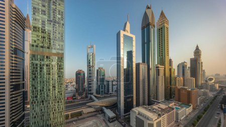 Téléchargez les photos : Vue aérienne panoramique du quartier financier international de Dubaï avec de nombreux gratte-ciel intemporels toute la journée. Trafic sur une route près de parking à plusieurs étages avec des ombres se déplaçant rapidement. Dubai, Émirats arabes unis. - en image libre de droit