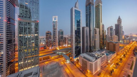 Téléchargez les photos : Panorama aérien du quartier financier international de Dubaï avec de nombreux gratte-ciel nuit à jour passage timelapse. Trafic sur une route près d'un parking à plusieurs étages avec piscine sur le toit. Dubai, Émirats arabes unis. - en image libre de droit