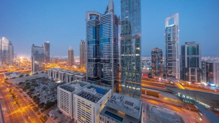 Foto de Vista panorámica aérea del Distrito Financiero Internacional de Dubái con muchos rascacielos noche a día timelapse transición. Tráfico en un cruce de carreteras en la carretera Sheikh Zayed antes del amanecer. Dubai, Emiratos Árabes Unidos. - Imagen libre de derechos