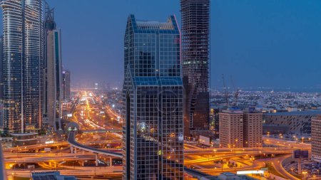 Téléchargez les photos : Vue panoramique de la ville de Dubaï avec métro et voitures se déplaçant sur l'autoroute la plus achalandée de la ville nuit aérienne à la transition de jour timelapse. Jonction entourée de gratte-ciel avant le lever du soleil - en image libre de droit