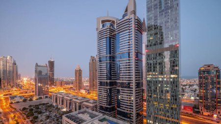 Téléchargez les photos : Vue aérienne du quartier financier international de Dubaï avec de nombreux gratte-ciels nuit à jour passage timelapse. Trafic sur une route près d'un parking avec des tours éclairées. Dubai, Émirats arabes unis. - en image libre de droit