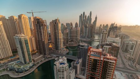Foto de Panorama de varios rascacielos en el bloque recidencial más alto de Dubai Marina durante el amanecer timelapse aéreo con canal artificial. Muchas torres y yates temprano en la mañana - Imagen libre de derechos