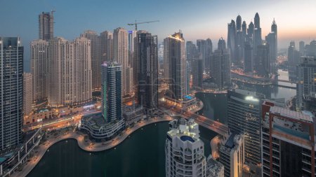 Foto de Vista de varios rascacielos en el bloque recidencial más alto de Dubai Marina y JBR distrito aéreo noche al día timelapse transición con canal artificial. Muchas torres y yates durante el amanecer - Imagen libre de derechos