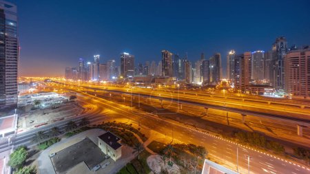 Téléchargez les photos : Dubai Marina gratte-ciel et Sheikh Zayed route avec métro ferroviaire aérienne nuit à jour transition timelapse panoramique. Trafic sur une autoroute près des tours modernes avant le lever du soleil, Émirats arabes unis - en image libre de droit