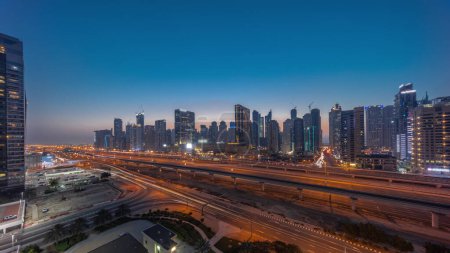 Téléchargez les photos : Dubai Marina gratte-ciel panorama et Sheikh Zayed route avec métro ferroviaire aérien jour à nuit passage timelapse. Trafic sur une autoroute près des tours modernes après le coucher du soleil, Émirats arabes unis - en image libre de droit
